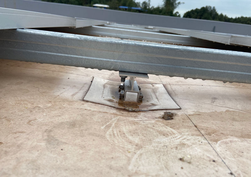 Traditional tpo roof base depression - Valin New Energy Low-angle view of a rooftop solar mounting rail system secured to a flat concrete roof with metal clamps fansing the structure.
